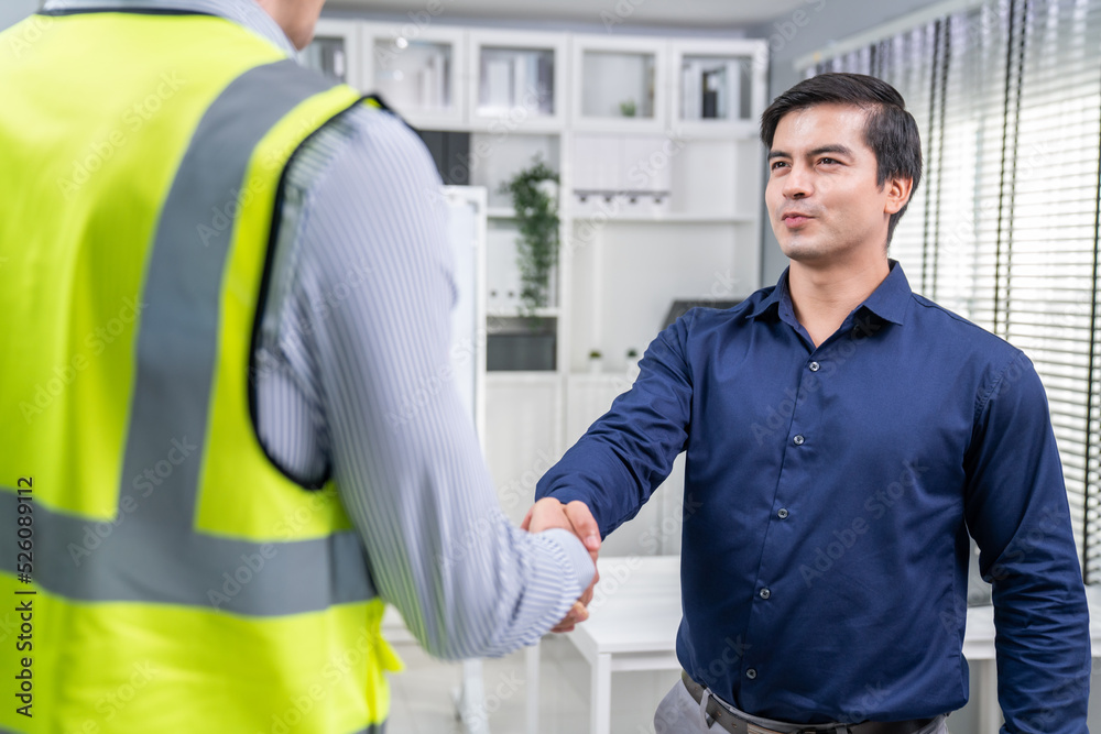 An engineer with a protective vest handshake with an investor in his office. Following a successful 