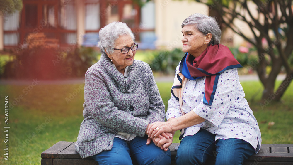 Two old women sitting on bench in park holding hands smiling happy life long friends enjoying retire