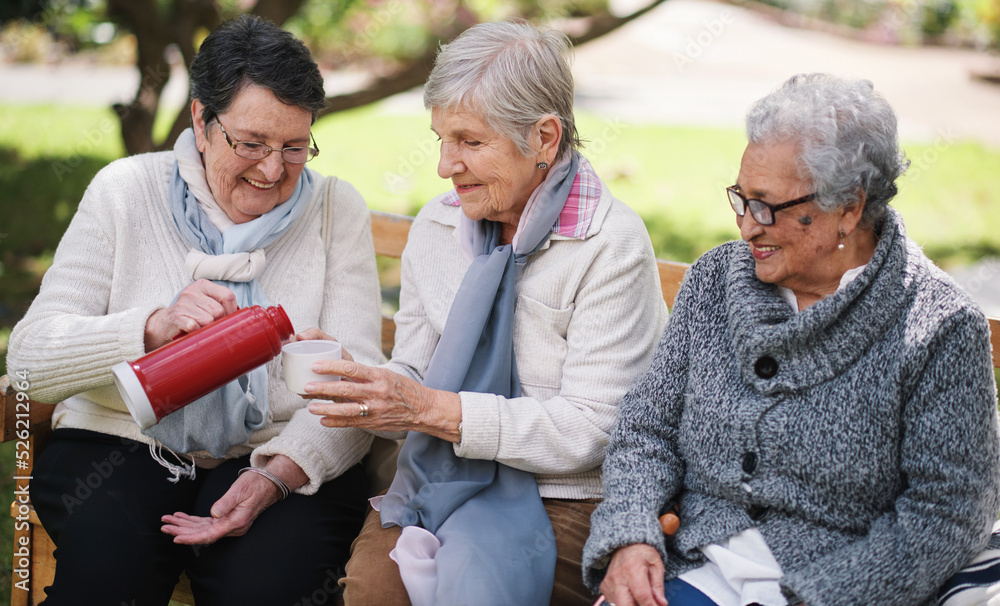 Happy old women sitting on bench in park drinkign tea enjoying retirement together