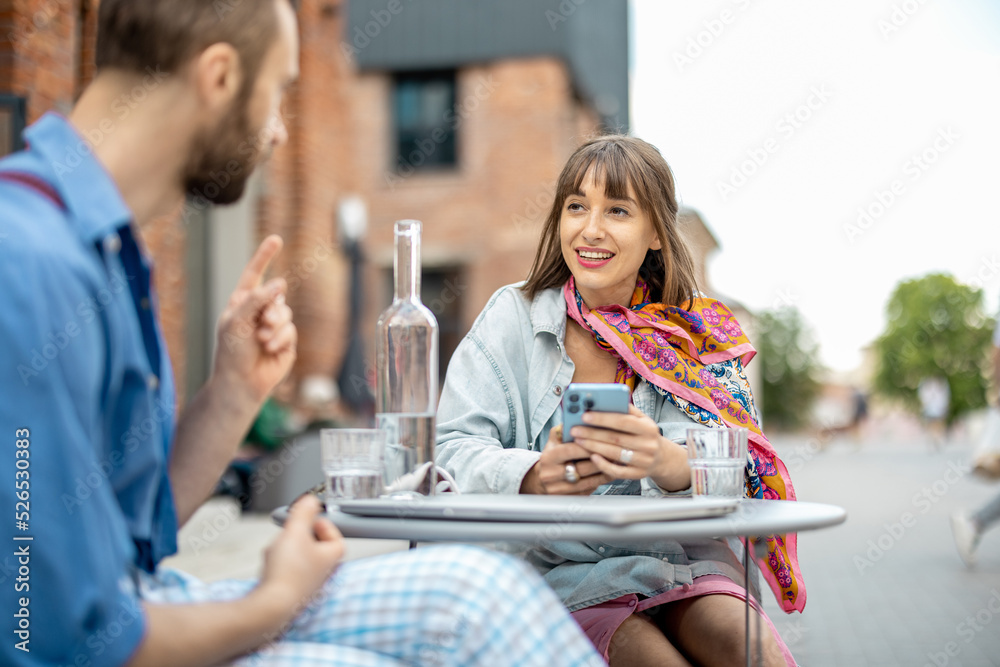 Stylish woman talks with his male colleague while sitting at cafe terrace outdoors. Business talk in