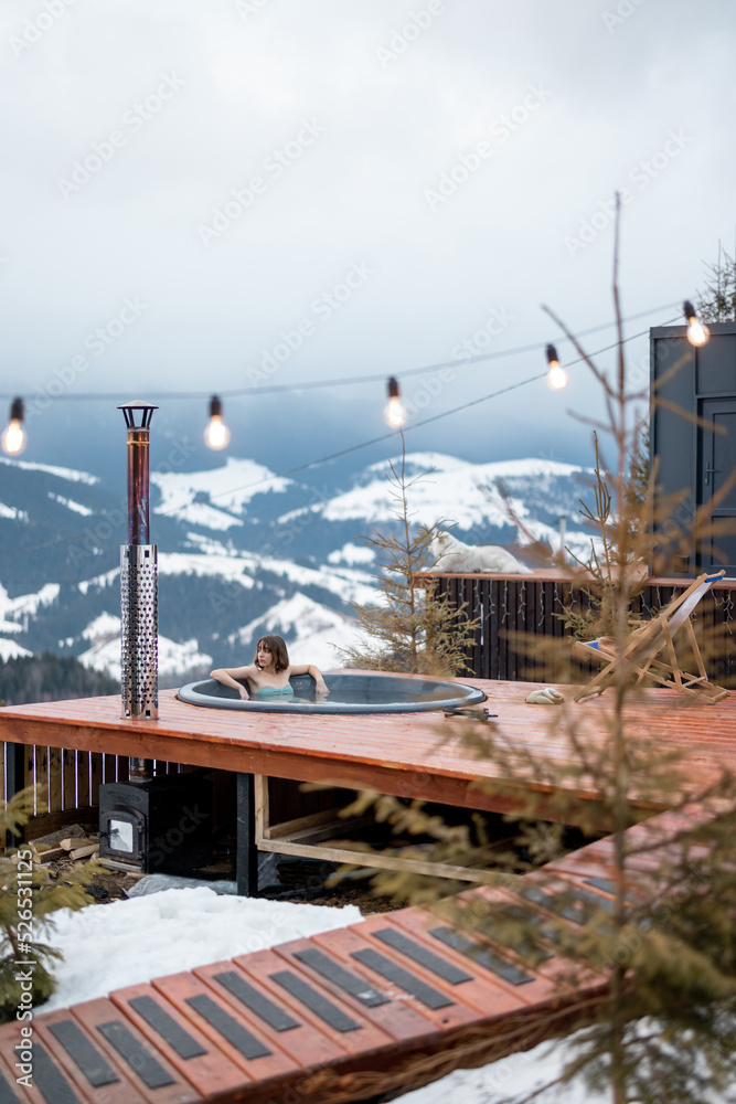 Woman swims in hot bath while resting at small modern house in the mountains on winter. Concept of r