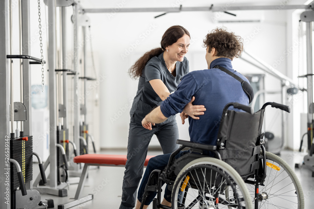 Rehabilitation specialist helps a guy stand out of a wheelchair at rehabilitation center. Concept of