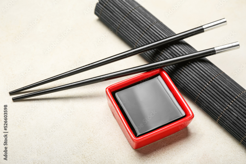 Red bowl of soy sauce, chopsticks and bamboo mat on white background