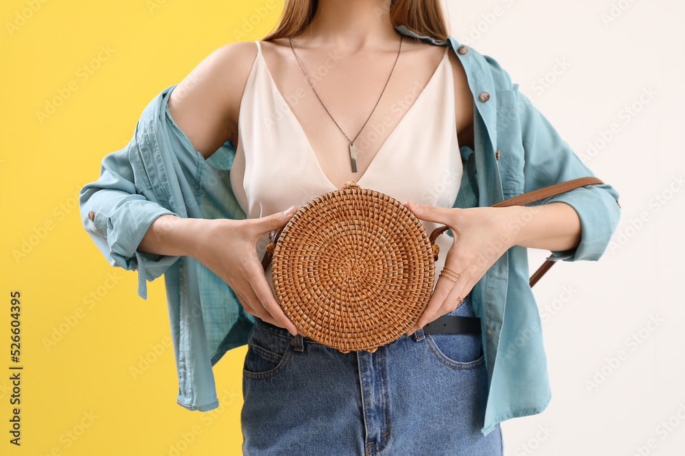 Woman holding rattan handbag on color background, closeup