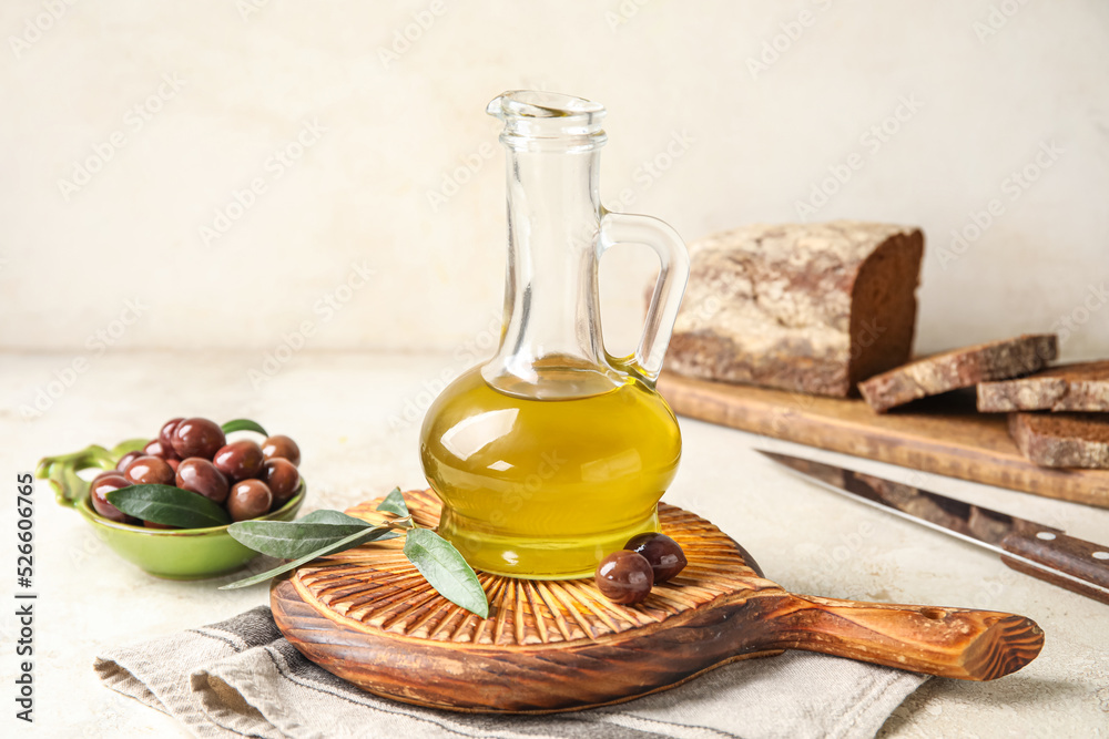 Wooden board with decanter of fresh olive oil on light background