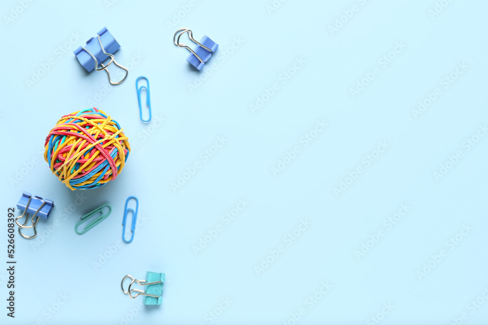 Colorful rubber band ball with paper clips on blue background