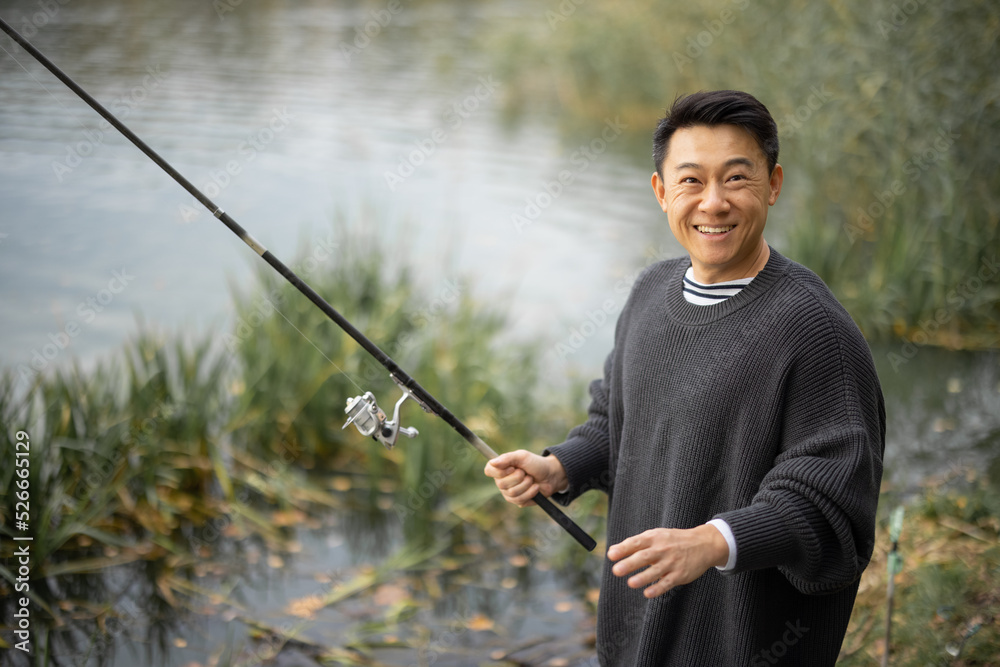 亚洲男子独自在河边或湖边钓鱼的肖像。休闲、爱好和周末的概念在