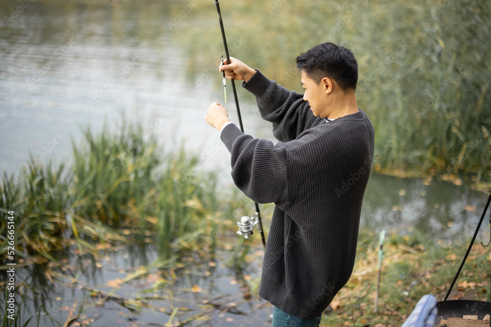 亚洲男子独自在河流或湖岸钓鱼。休闲、爱好和周末在大自然中的概念。Aut