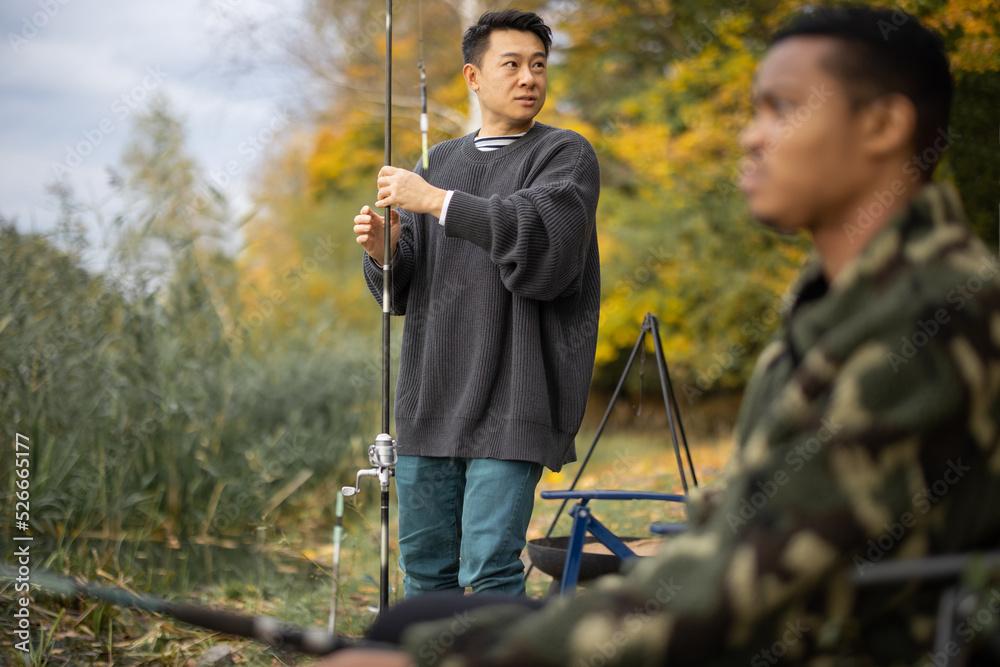 Two multiracial male friends fishing in nature. Men resting and spending time together on river or l