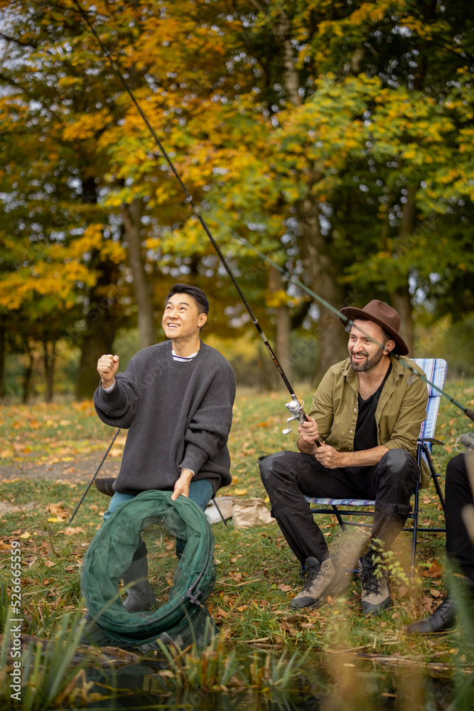 Pleased multiracial male friends resting and fishing on river or lake coast. Concept of leisure, hob