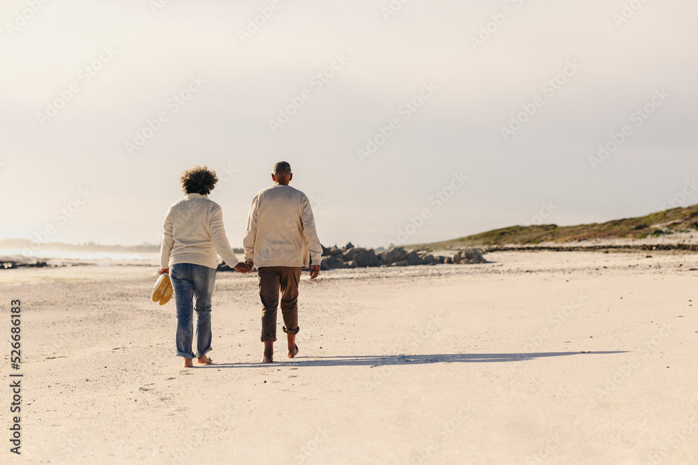 Rearview of an elderly couple walking barefoot on beach sand