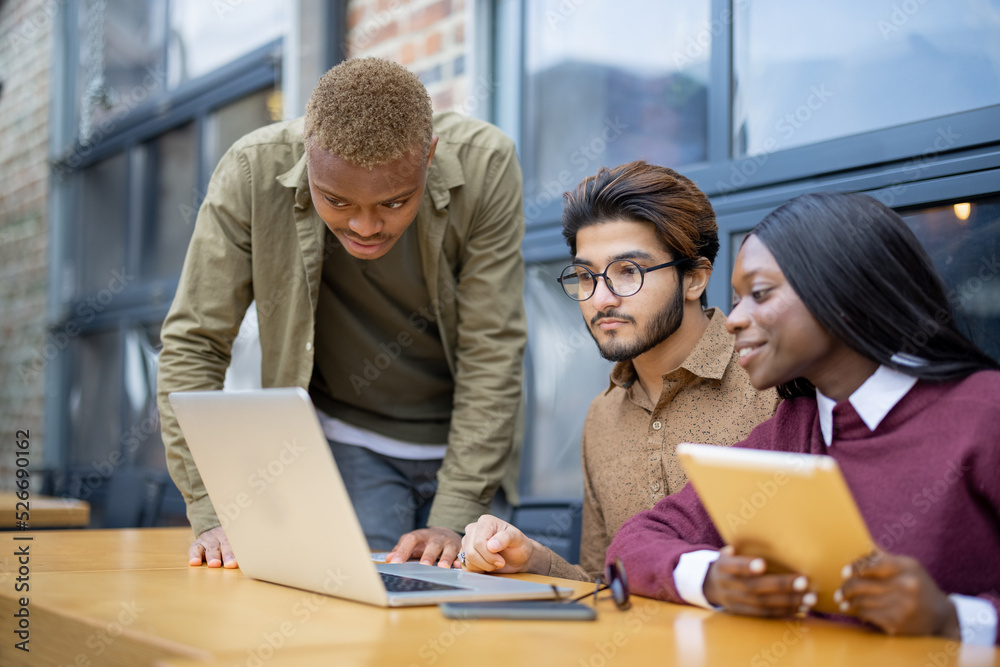 Multiracial students watching something on laptop while sitting at table outdoors. Concept of remote