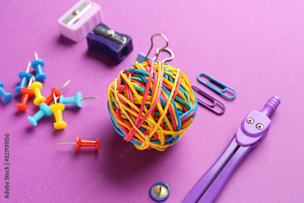 Colorful rubber band ball and stationery supplies on purple background