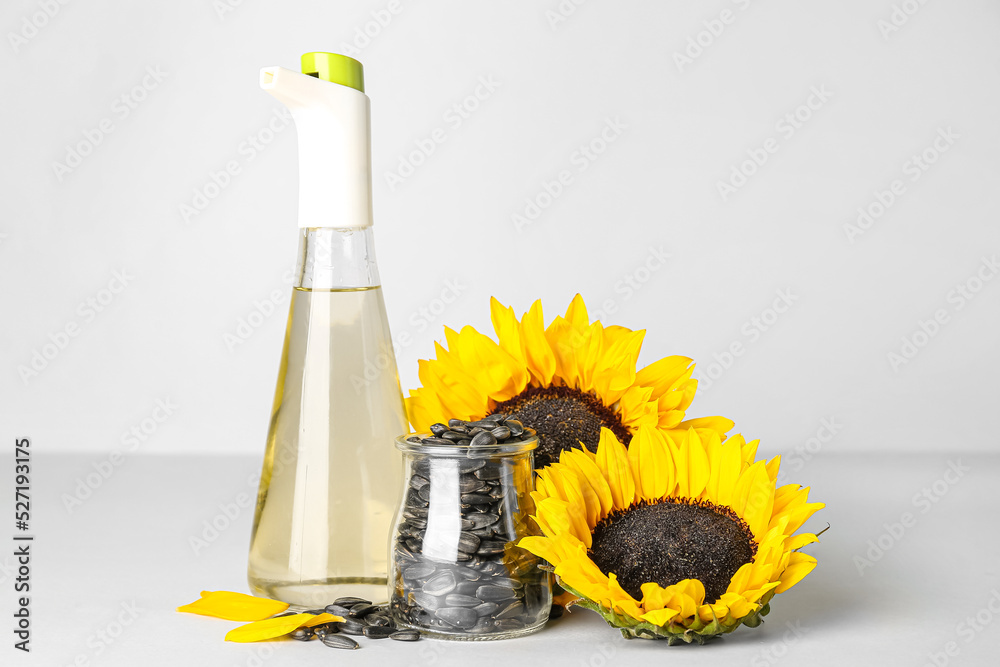 Sunflowers with seeds and bottle of oil on light background