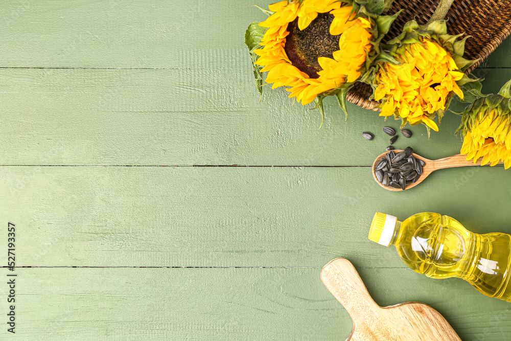 Bottle of oil, sunflowers, spoon with seeds and board on green wooden background