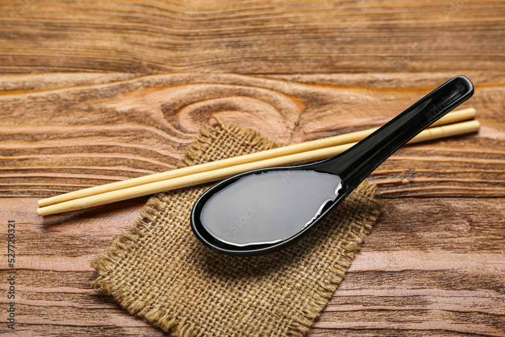 Spoon of soy sauce, chopsticks and sack cloth on wooden background