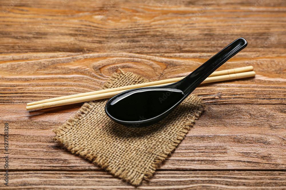 Spoon of soy sauce, chopsticks and sack cloth on wooden background