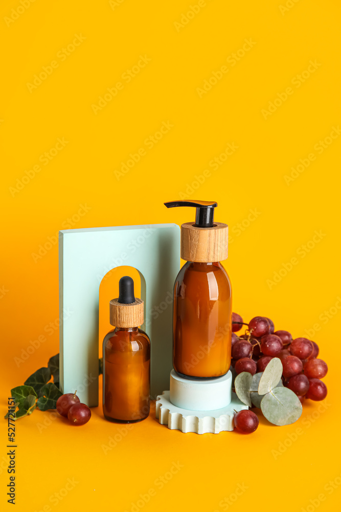 Composition with bottles of natural cosmetic products, grapes and plaster decor on color background