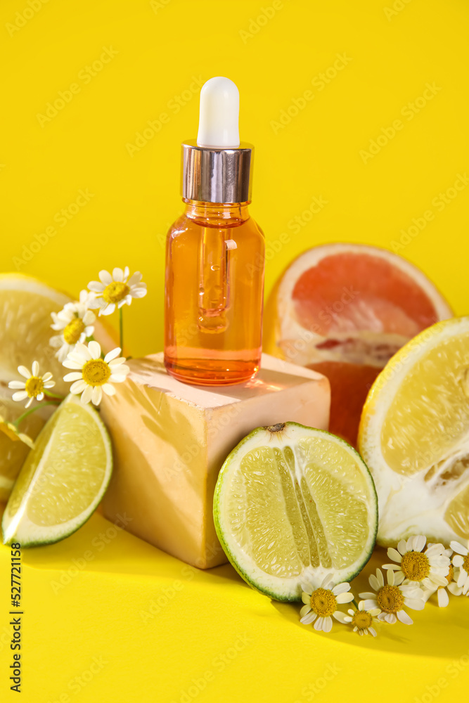 Composition with bottle of essential oil, citrus fruits and chamomile flowers on yellow background, 