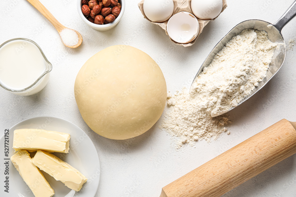 Raw dough with ingredients and utensils on white background