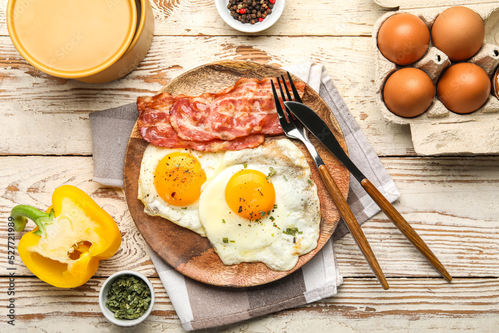 Plate of tasty fried eggs with bacon and ingredients on light wooden background