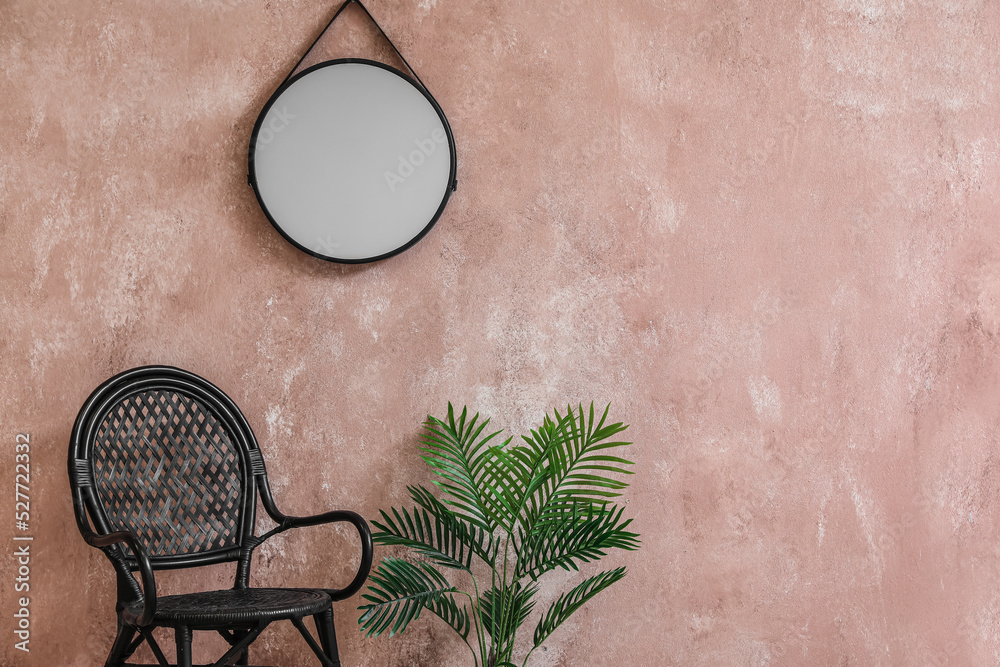 Stylish chair, houseplant and mirror hanging on pink wall