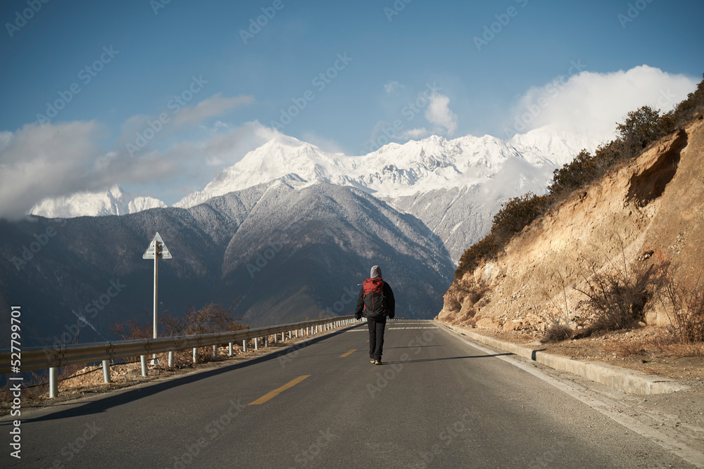 亚洲徒步背包客走在高速公路上，背景是雪山