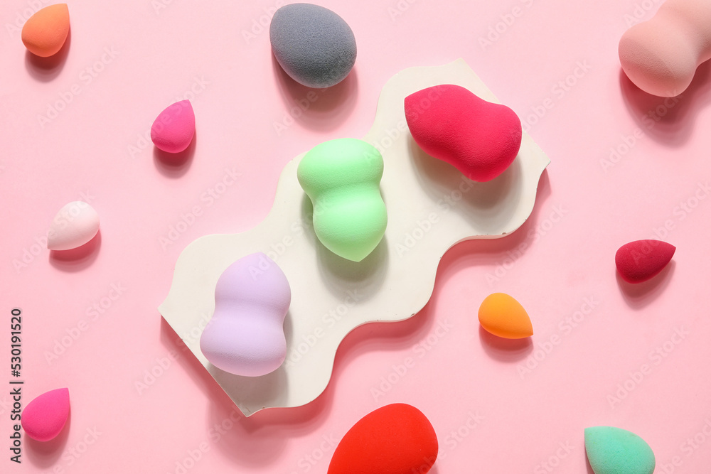 Stand with colorful makeup sponges on pink background