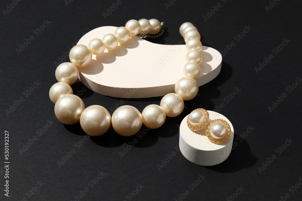 Showcase pedestals with elegant pearl jewelry on black background