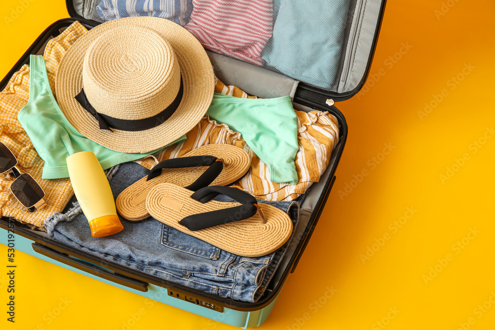 Open suitcase with beach accessories and clothes on color background, closeup