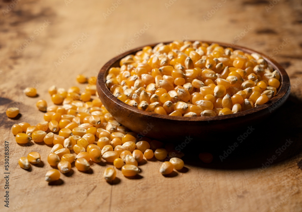 Dried corn kernels in a wooden bowl placed against a wooden background.