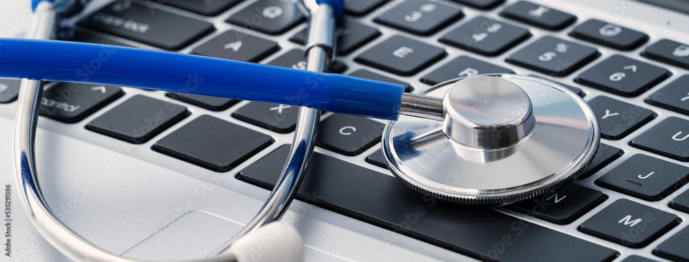 Blue stethoscope on laptop computer keyboard, medical design concept.