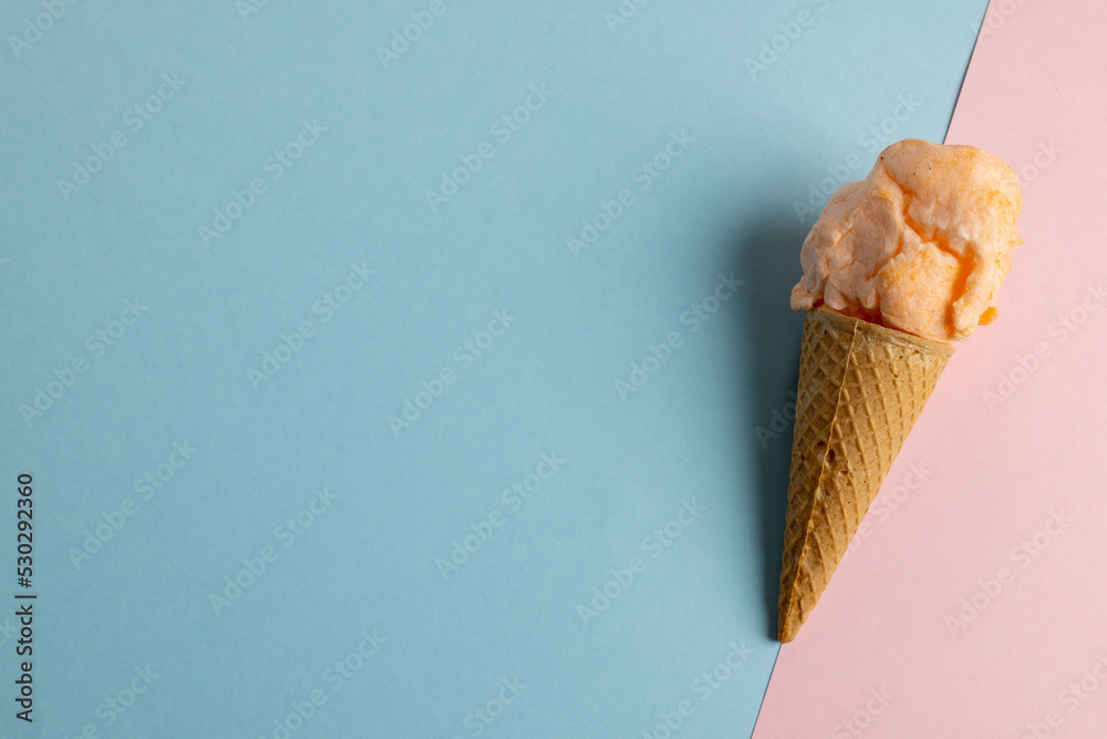 Horizontal image of orange homemade ice cream in cone, on blue and pink with copy space