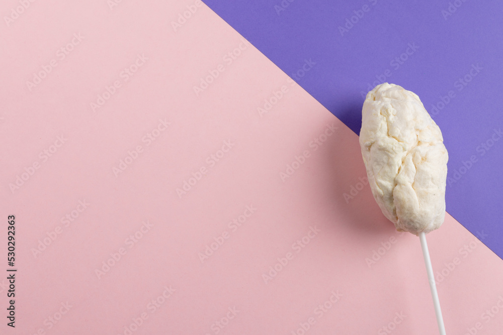 Horizontal image of homemade white candy floss on stick, on pink and purple with copy space