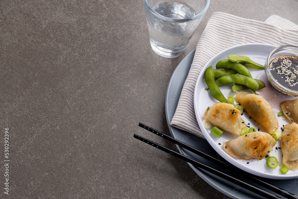 Overhead view of asian dumplings, soy sauce and chopsticks with glass of water on grey background