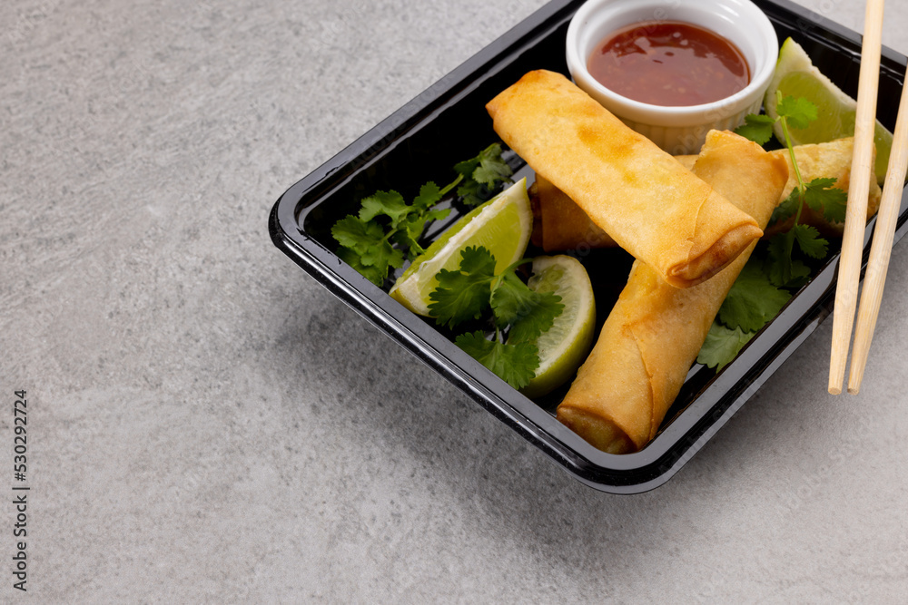 Overhead view of asian spring rolls, sliced lime, chilli sauce and chopsticks on grey background