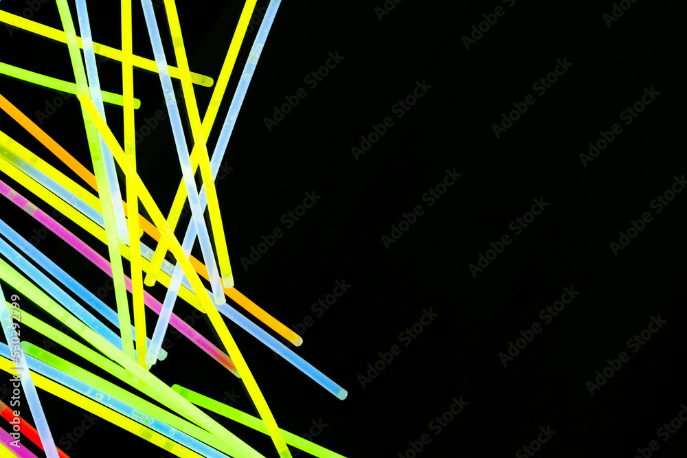 Image of vibrant stack of neon glow sticks scattered over black background with copy space