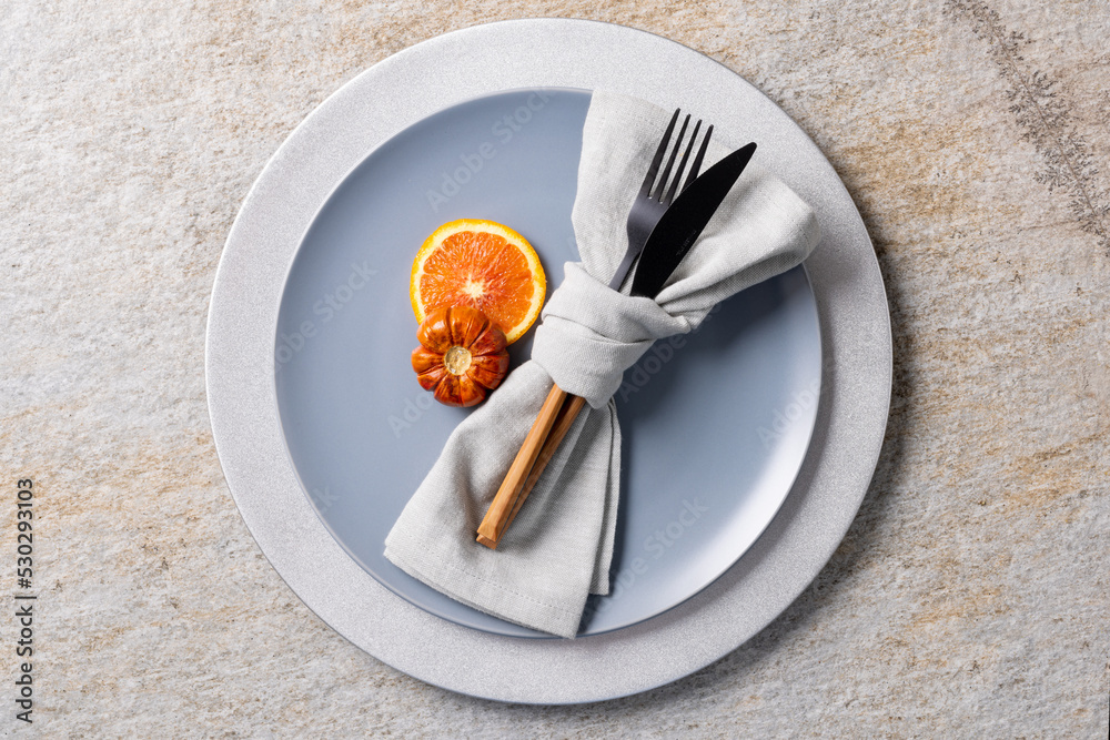 Overhead view of plate and cutlery with autumn decoration and copy space on grey background