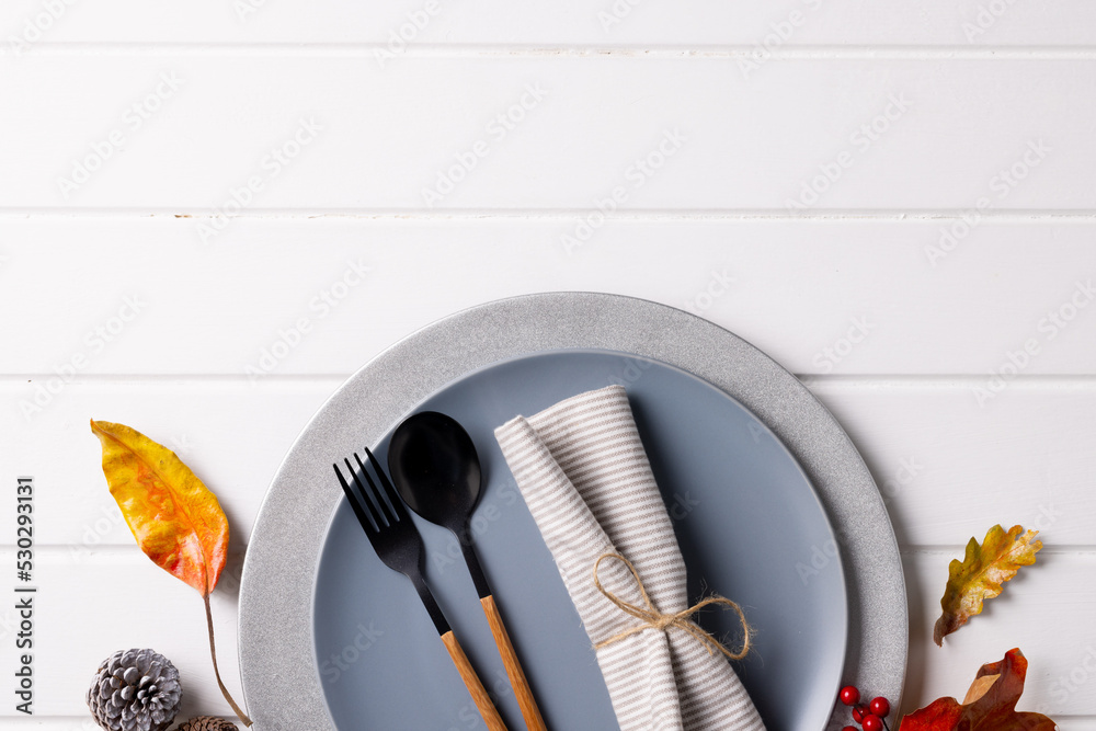 Overhead view of plate and cutlery with autumn decoration and copy space on wooden background