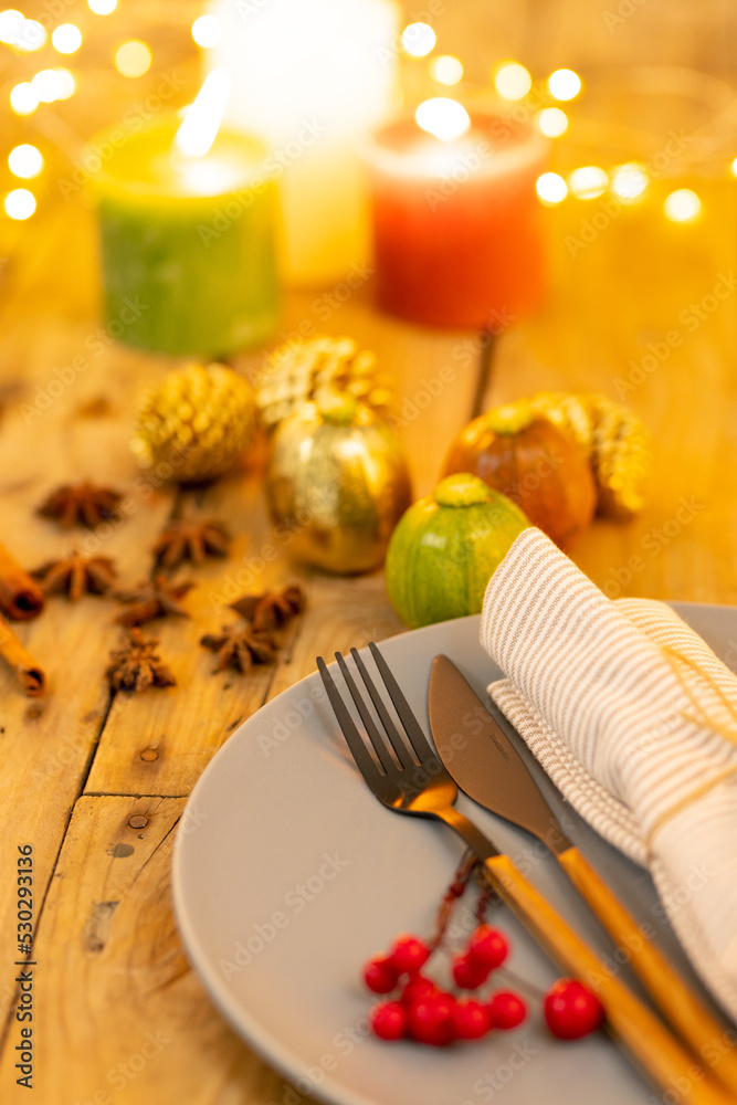 Overhead view of plate and cutlery with autumn decoration and candles on wooden background