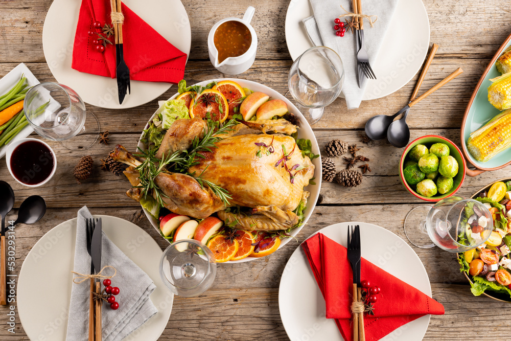 Overhead view of thanksgiving table with roast chicken and vegetables and autumn decoration on wood