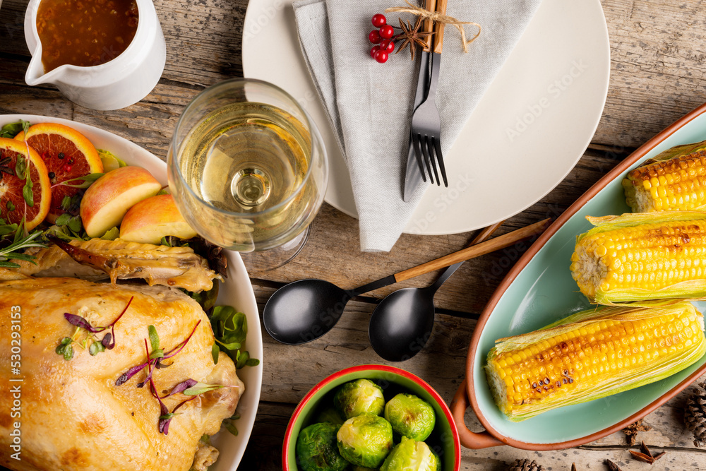 Overhead view of thanksgiving table with roast chicken and vegetables and autumn decoration on wood