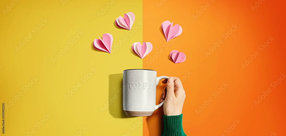 Female hand holding a mug with paper craft hearts - flat lay