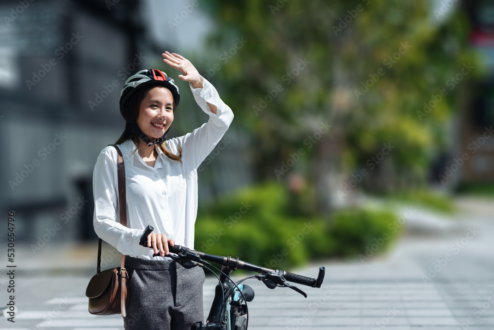 年轻的亚洲女商人戴着头盔，骑着自行车站在城市街道上看天空