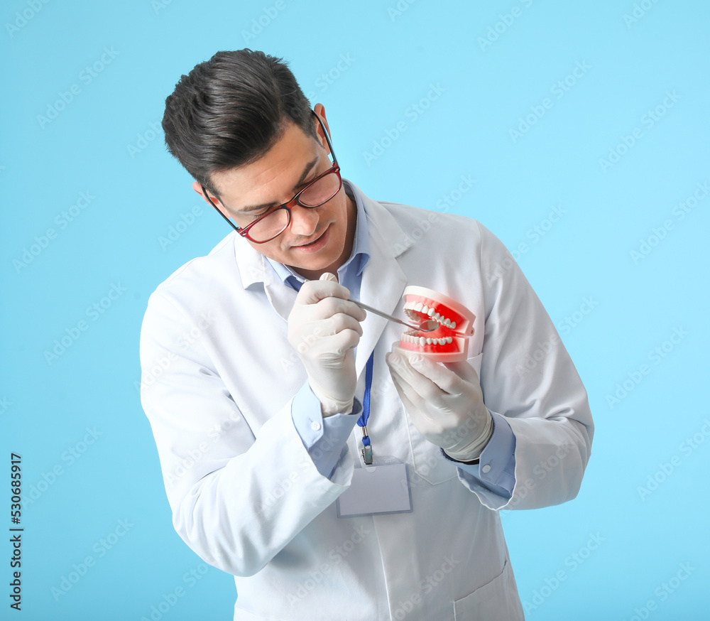 Male dentist with plastic jaw model on blue background