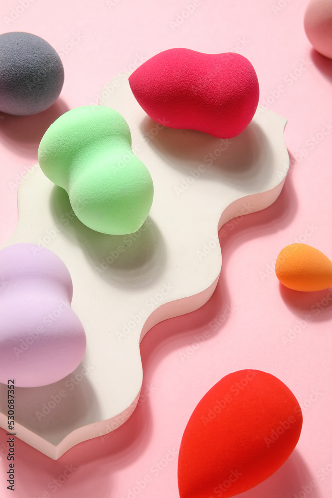 Stand with colorful makeup sponges on pink background