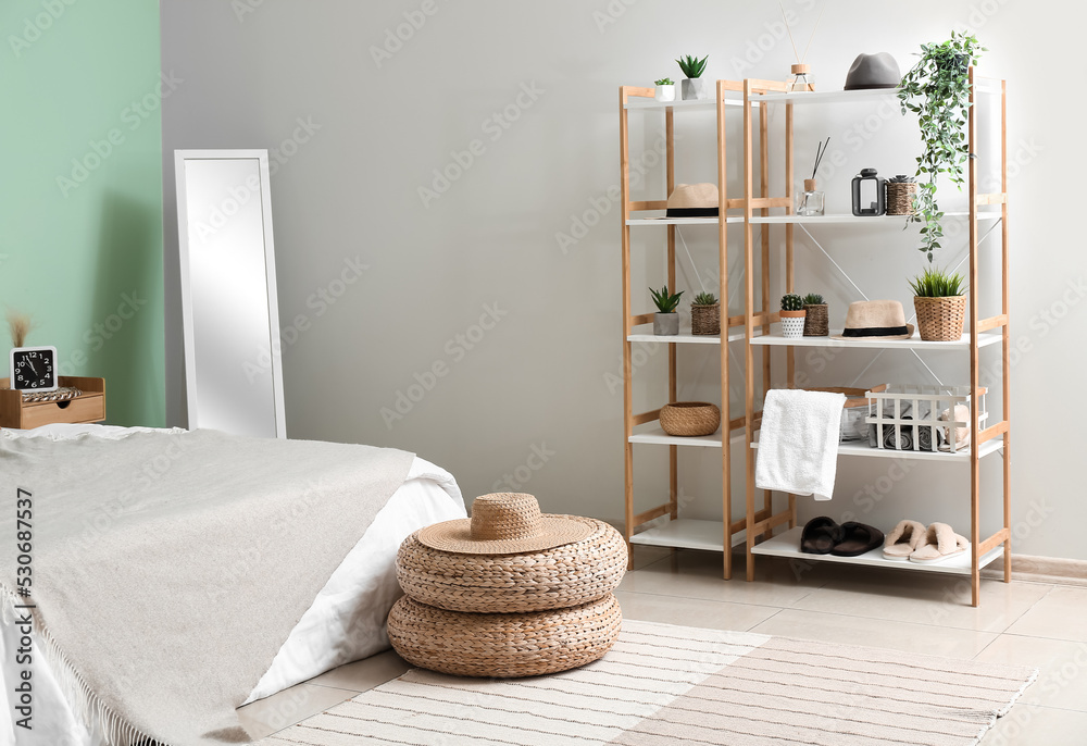 Interior of cozy bedroom with rattan poufs, mirror and shelving unit