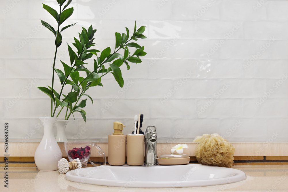 Bath accessories, sink, vase with plant branches and flower on table in bathroom