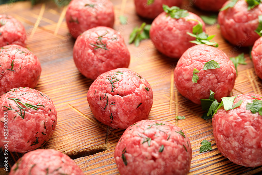 Raw meat balls with cut herbs on wooden board, closeup