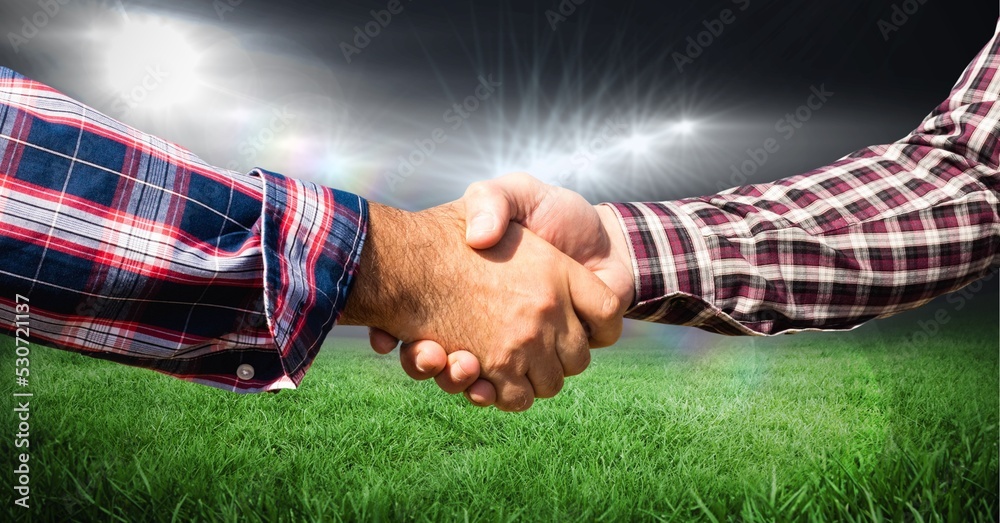 Composition of two businessmen shaking hands over sports stadium